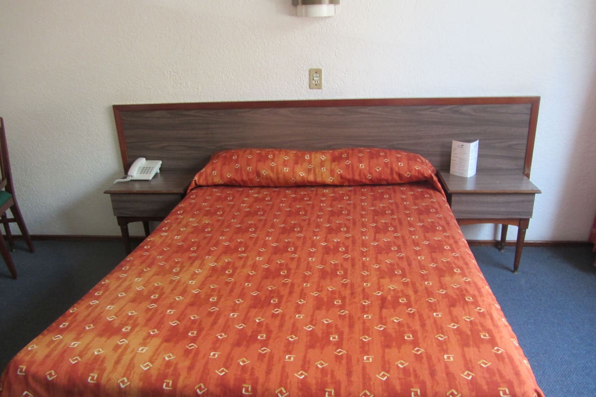A hotel room with a single bed, a bedside table, a chair, and a wall-mounted telephone.