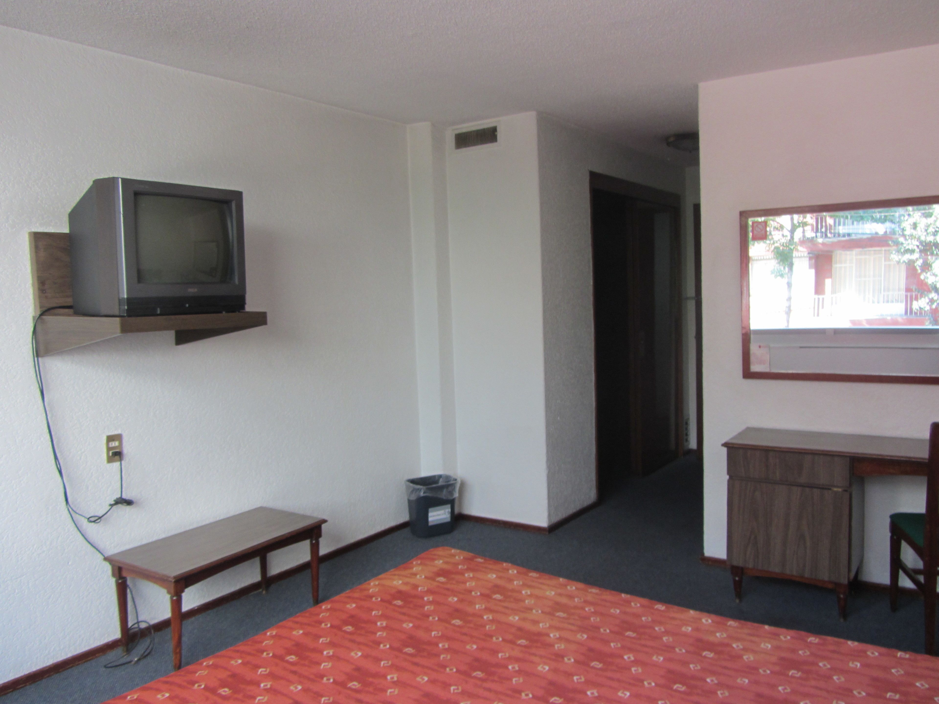A room with a bed, a desk, a television on a shelf, and a window.