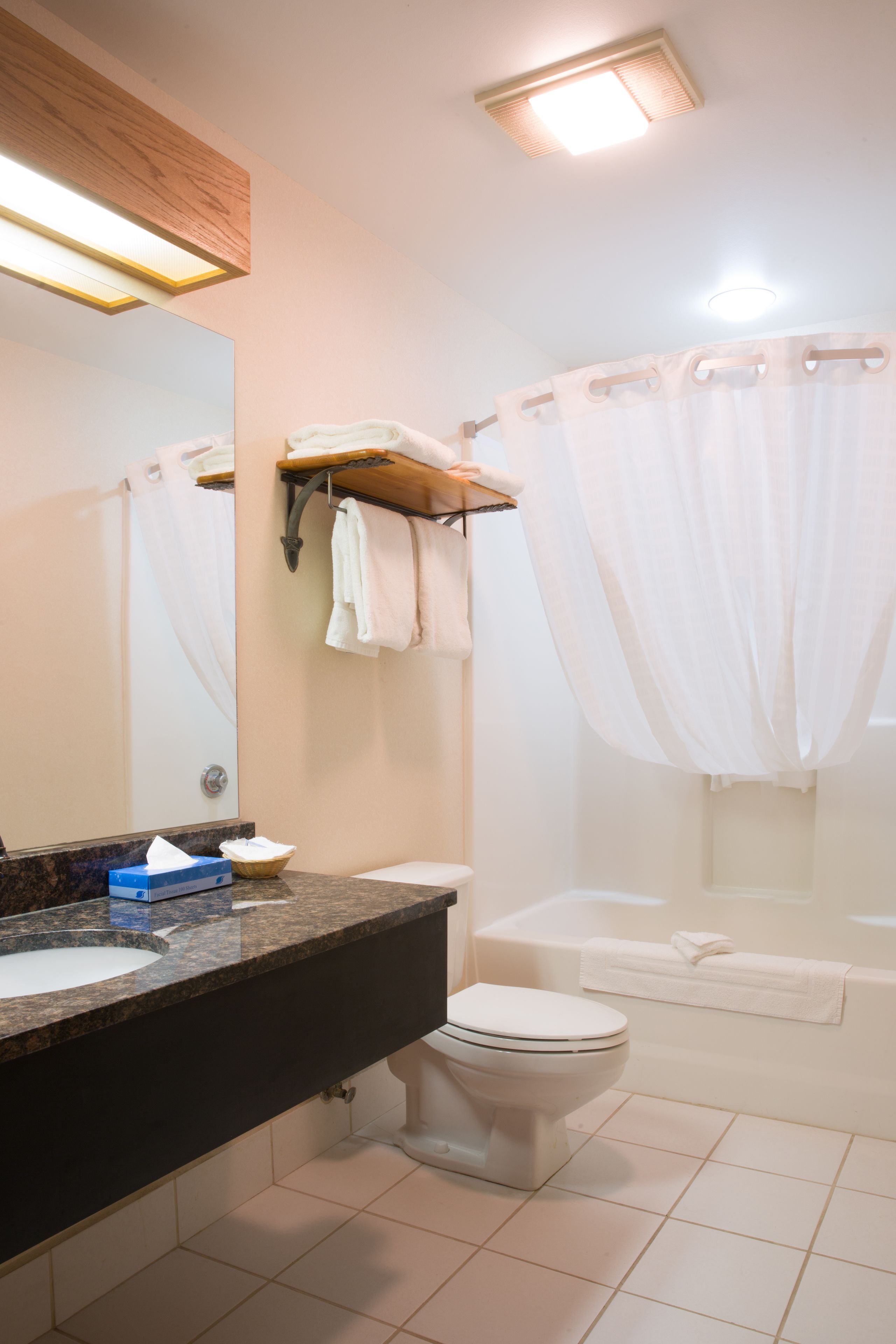 A bathroom with a toilet, sink, and bathtub. There is a towel rack with towels and a shower curtain.
