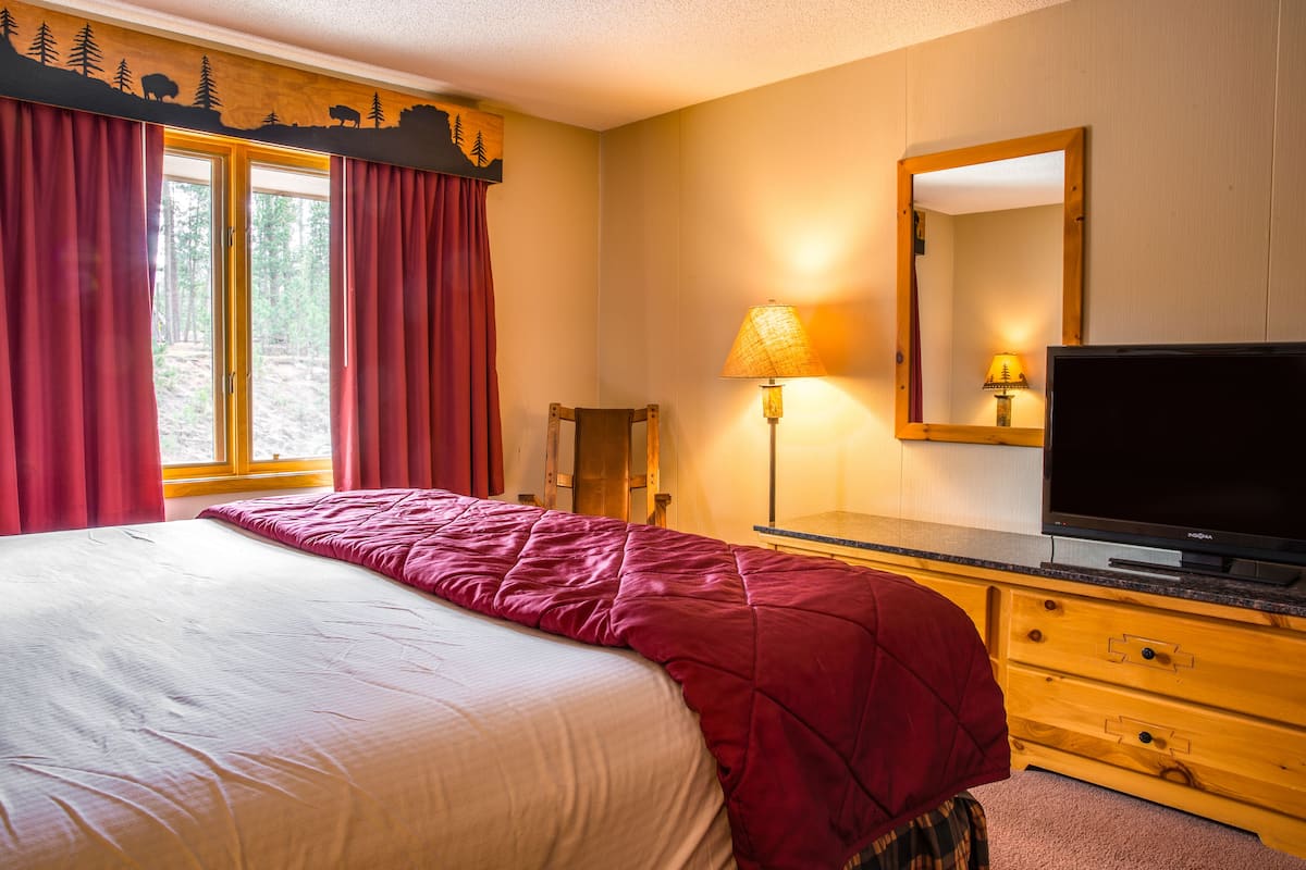 Een slaapkamer met een bed, een televisie, een lamp, een dressoir en een raam met gordijnen.