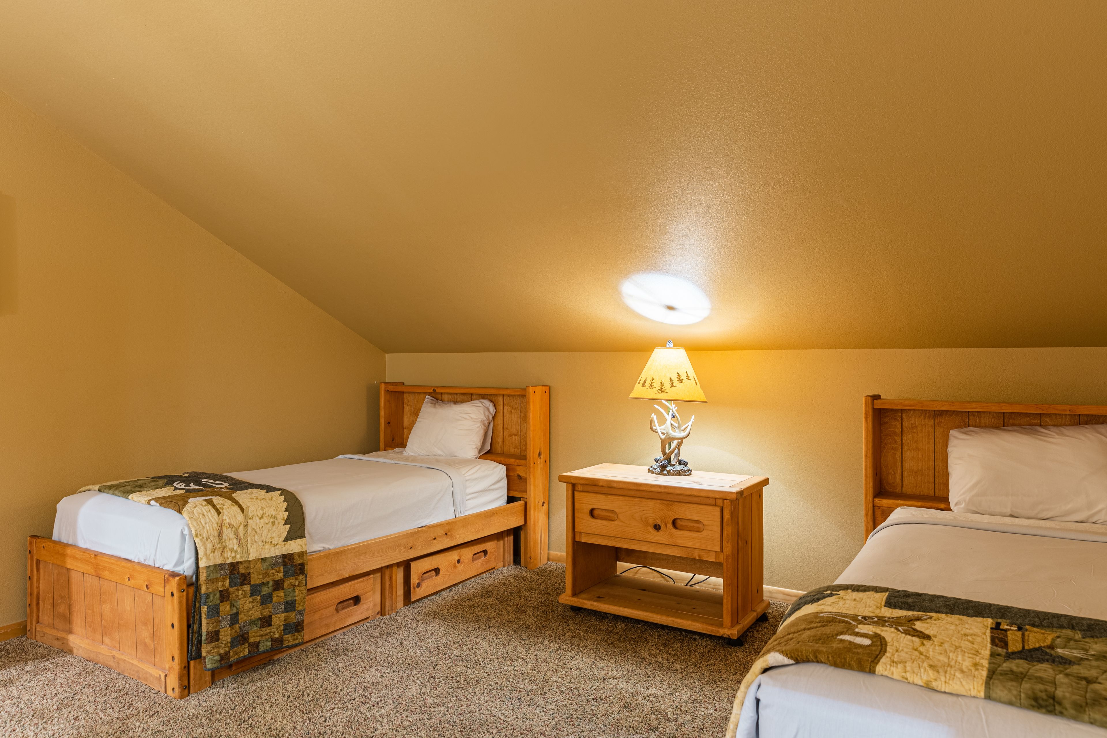 A bedroom with two wooden beds, a nightstand with a lamp, and a carpeted floor.