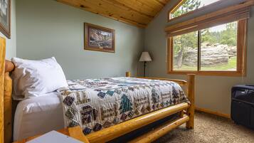 A wooden bed with a quilt, a bedside table with a notebook, a lamp, and a suitcase.