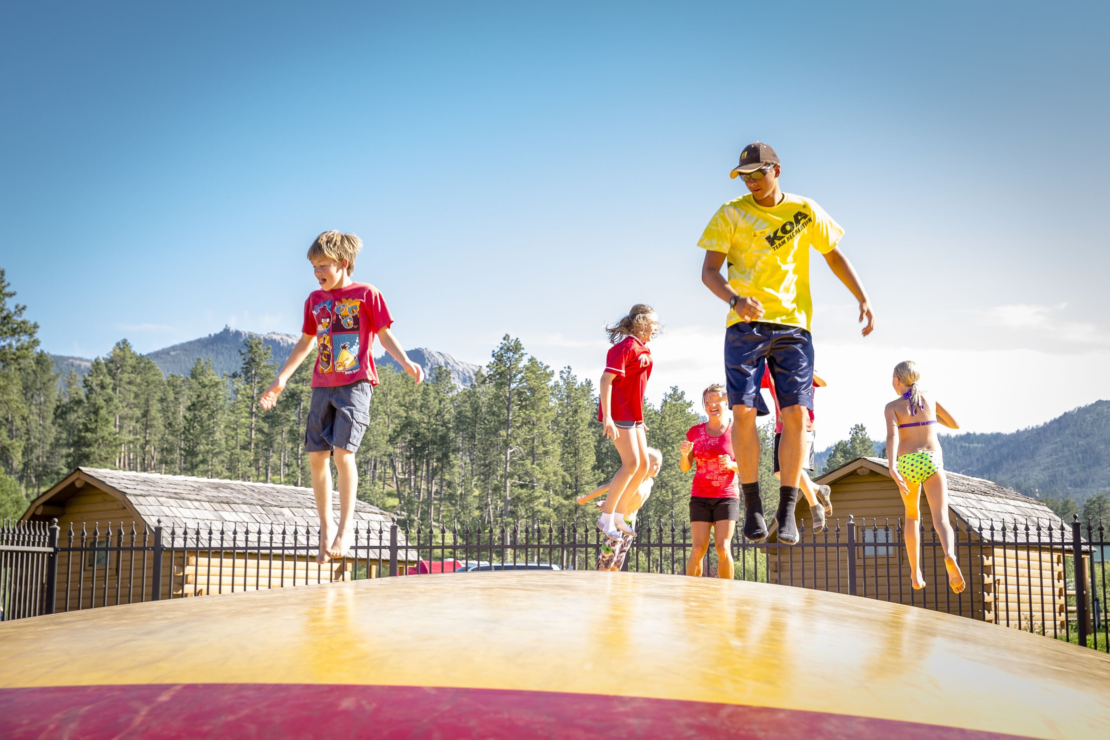 A group of people jumping on a wooden platform with a mountainous background.