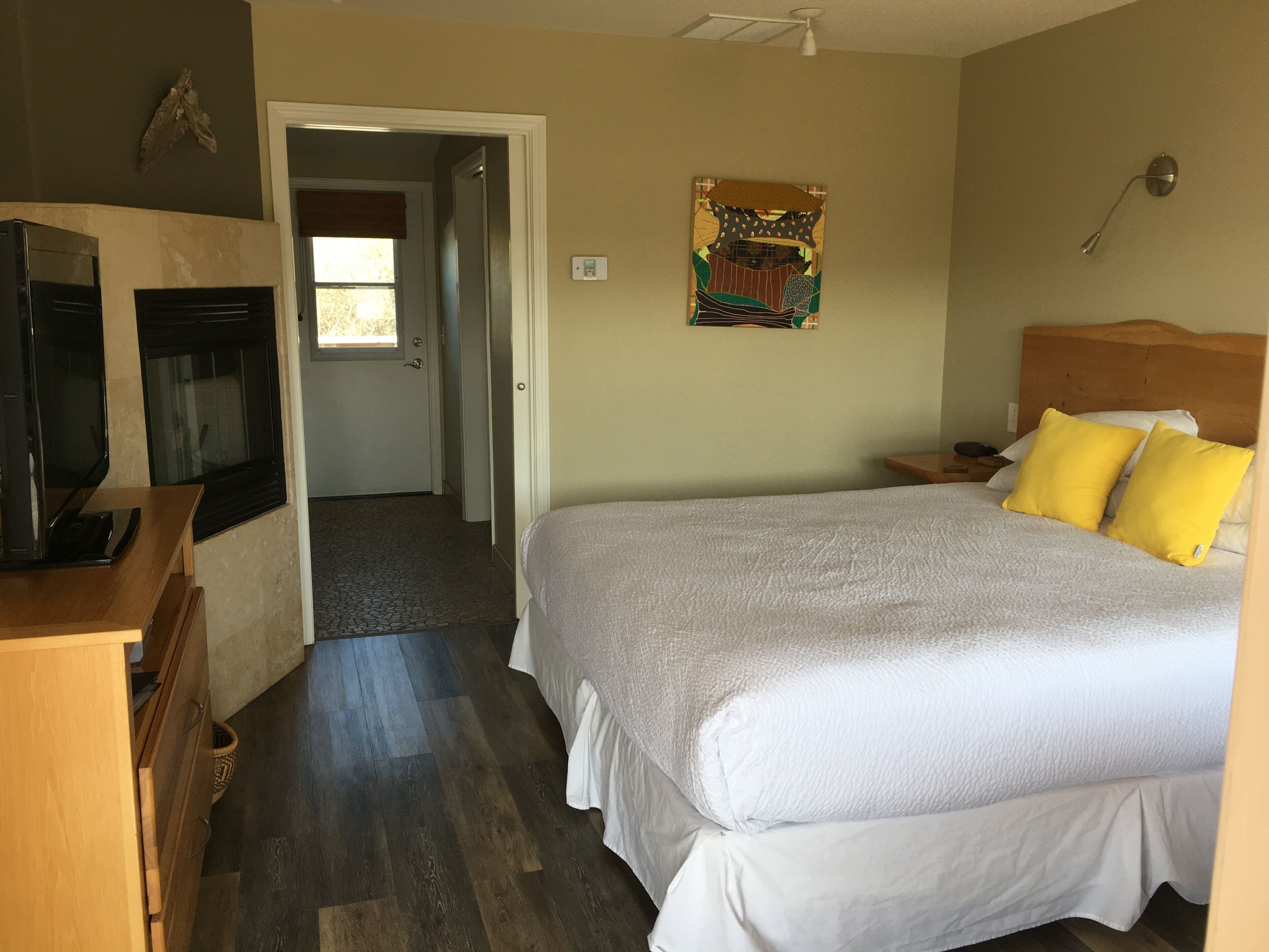 A bedroom with a large bed, a wooden dresser, a television, and a door leading to another room.