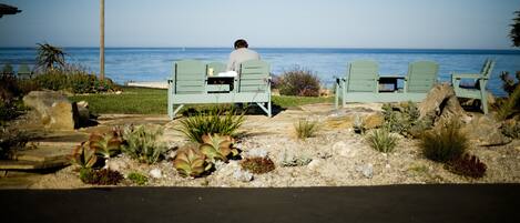 A person sitting on a chair facing the ocean, with a chair and table set up nearby.