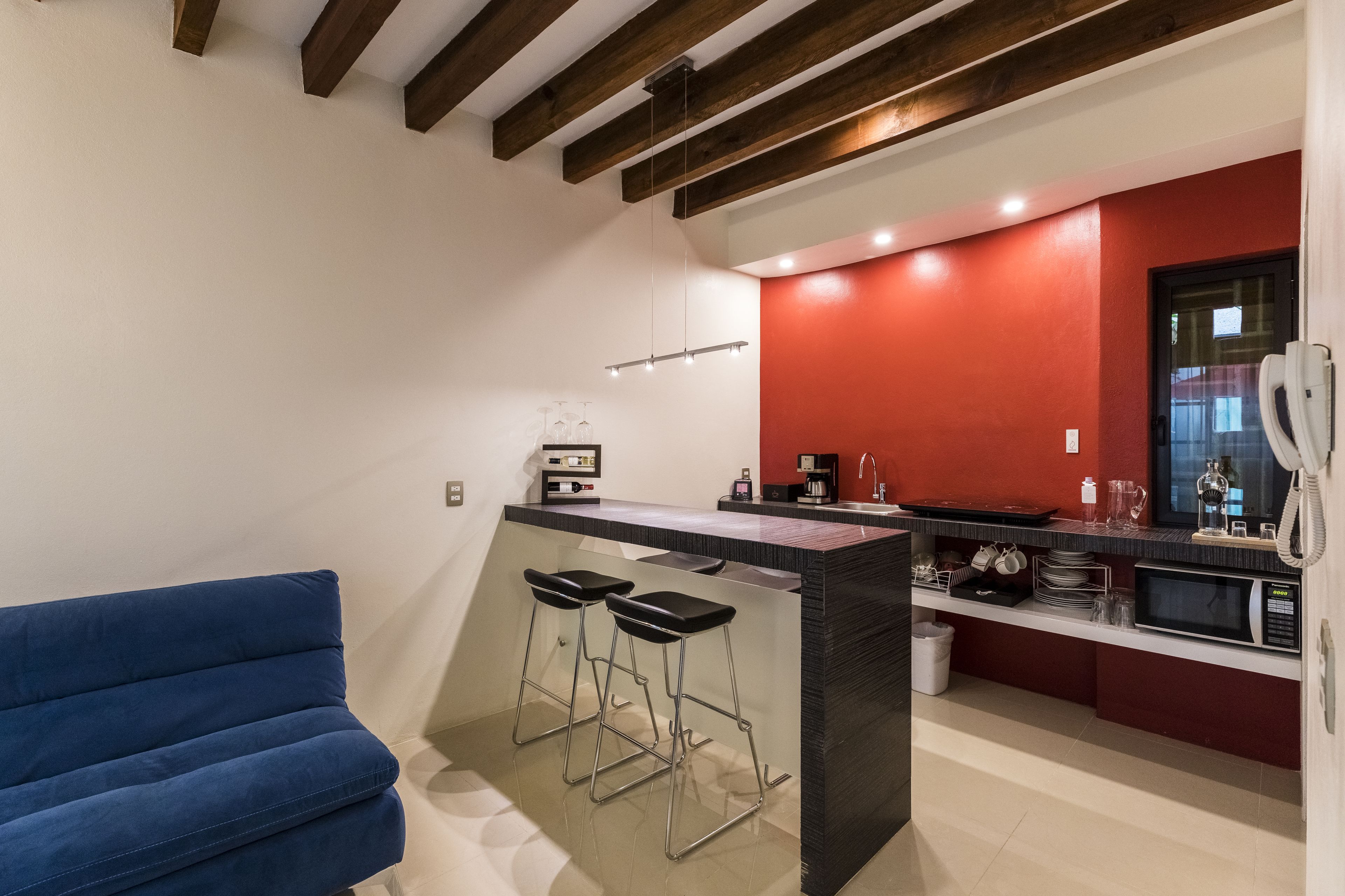 Une cuisine moderne avec un mur d’accent rouge, un coin bar avec des tabourets et un canapé bleu.