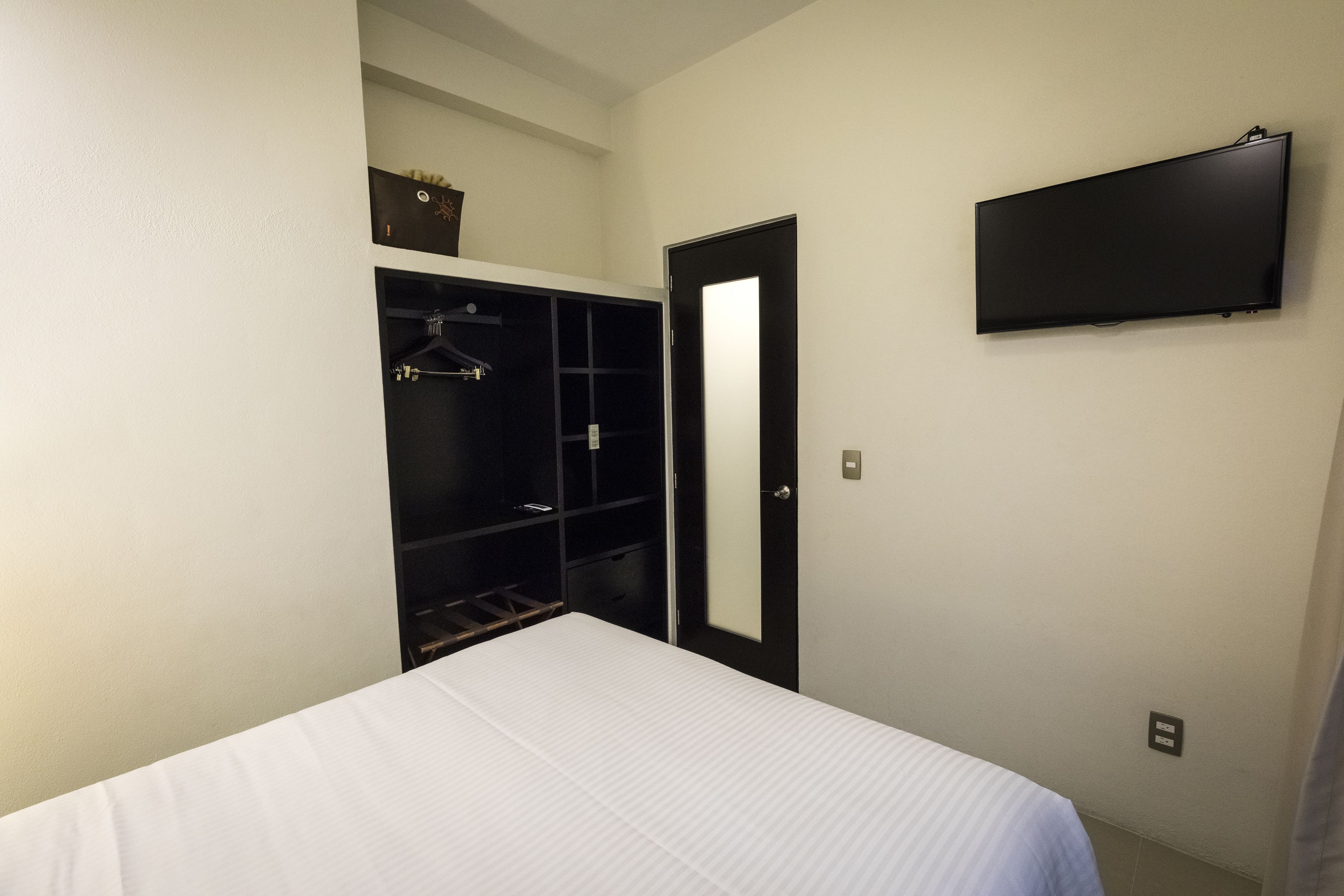 A bedroom with a bed, a wardrobe, and a TV mounted on the wall.