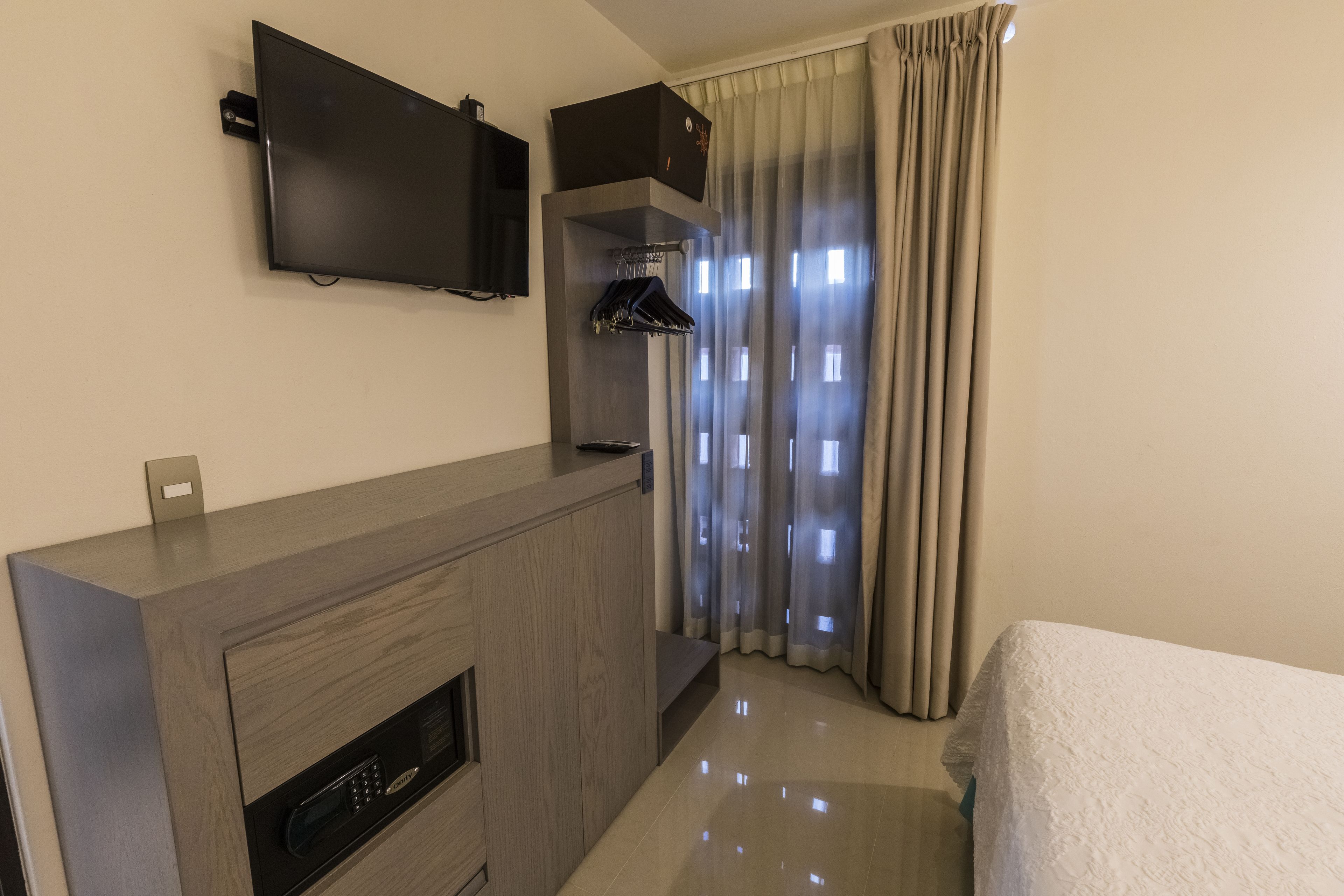 Une chambre d’hôtel dotée d’un téléviseur à écran plat fixé au mur, d’un meuble en bois intégré comprenant un micro-ondes, et d’un lit recouvert d’une couette blanche.