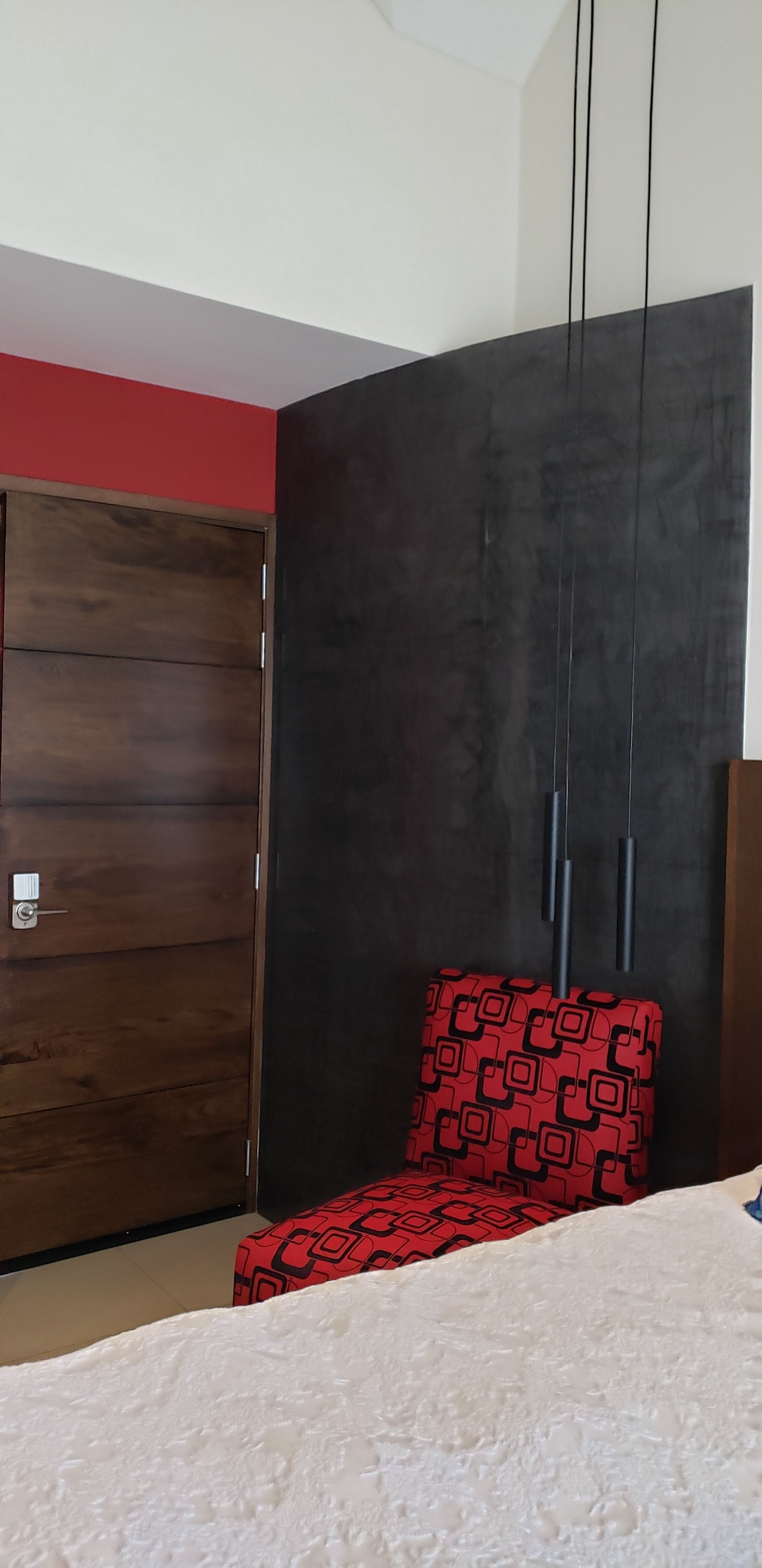 A bedroom with a large wardrobe, a red patterned chair, and a white bedspread.