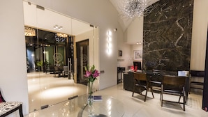 A modern hotel lobby with a glass table, seating area, and a marble wall.