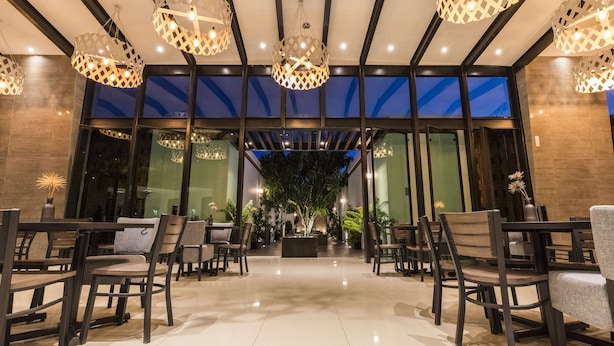 A modern indoor dining area with a central seating arrangement, large windows, and decorative lighting fixtures.