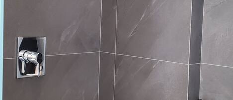 A modern shower area with dark tiles, a handheld showerhead, and a small shelf with toiletries.