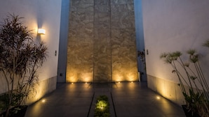 A modern building entrance with a textured wall, ambient lighting, and potted plants.
