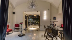 A modern hotel lobby with a glass coffee table, red chairs, a reception desk, and a chandelier.
