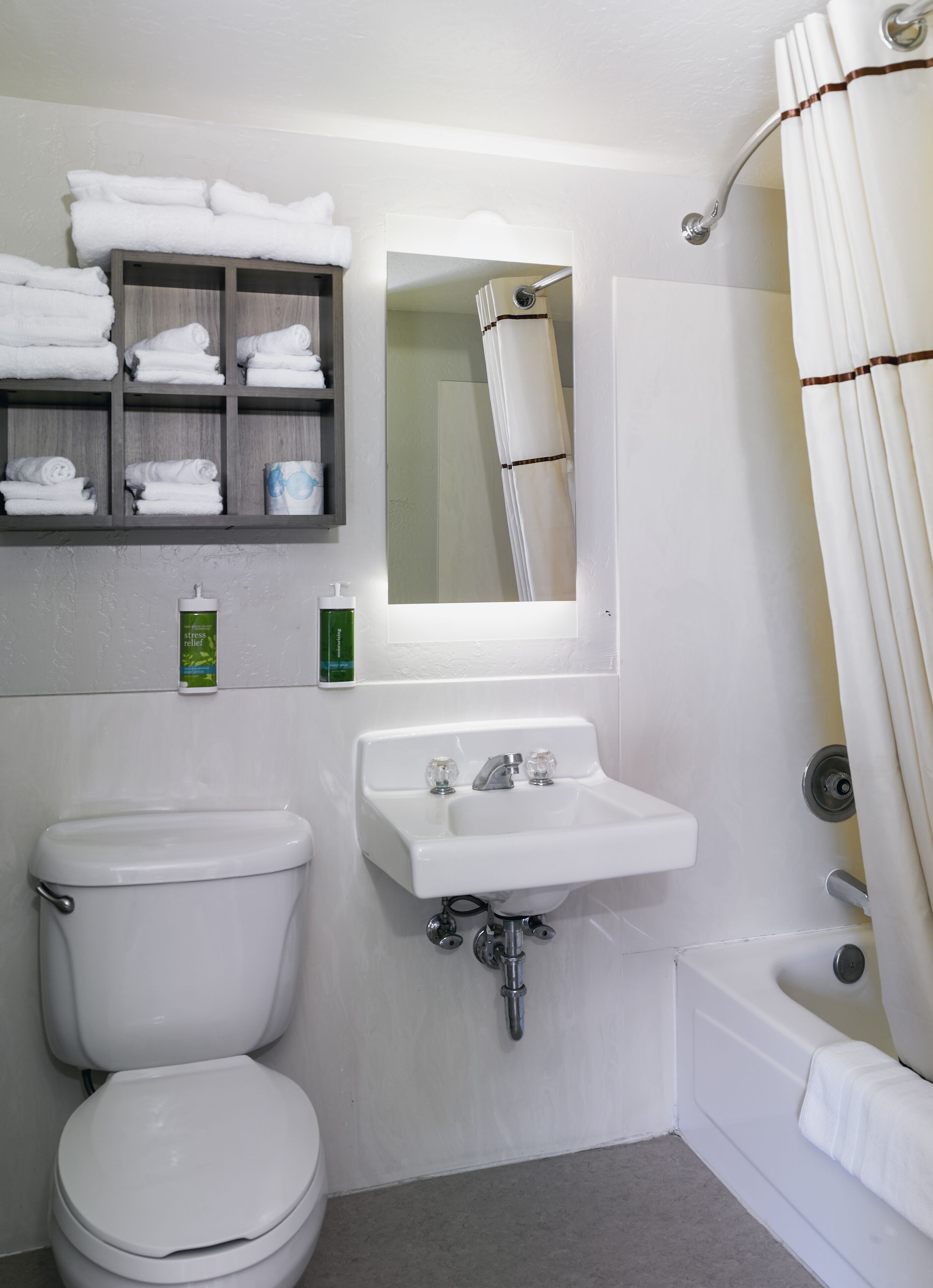 A bathroom with a toilet, sink, and bathtub. There are towels on a shelf and a shower curtain.