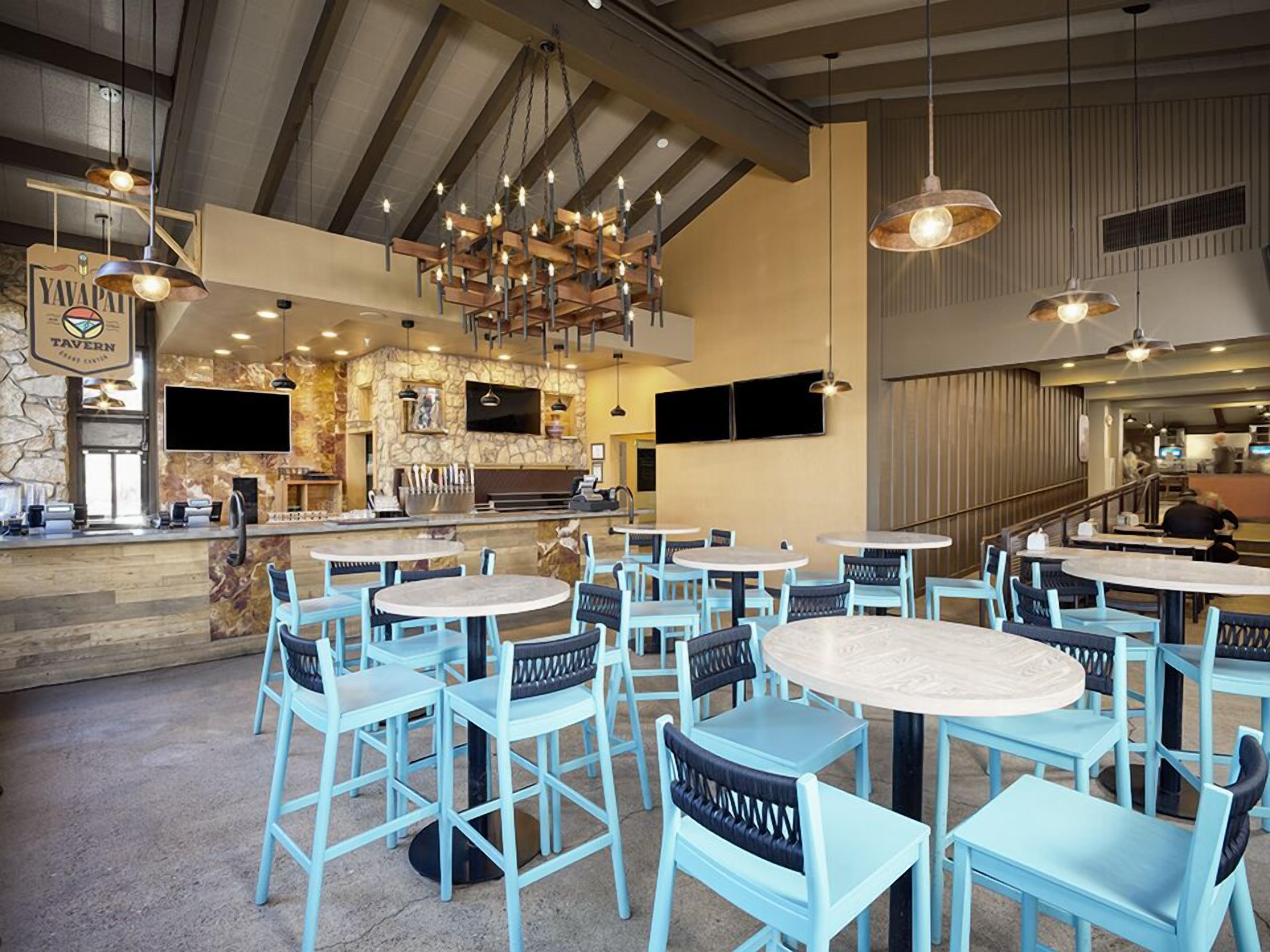 A restaurant interior with round tables and blue chairs, a stone wall, a bar area, and hanging pendant lights.