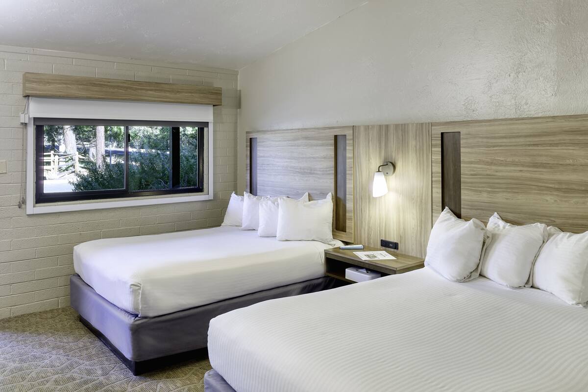 Habitación de hotel con dos camas, una ventana, una mesita de noche y una lámpara fijada a la pared.