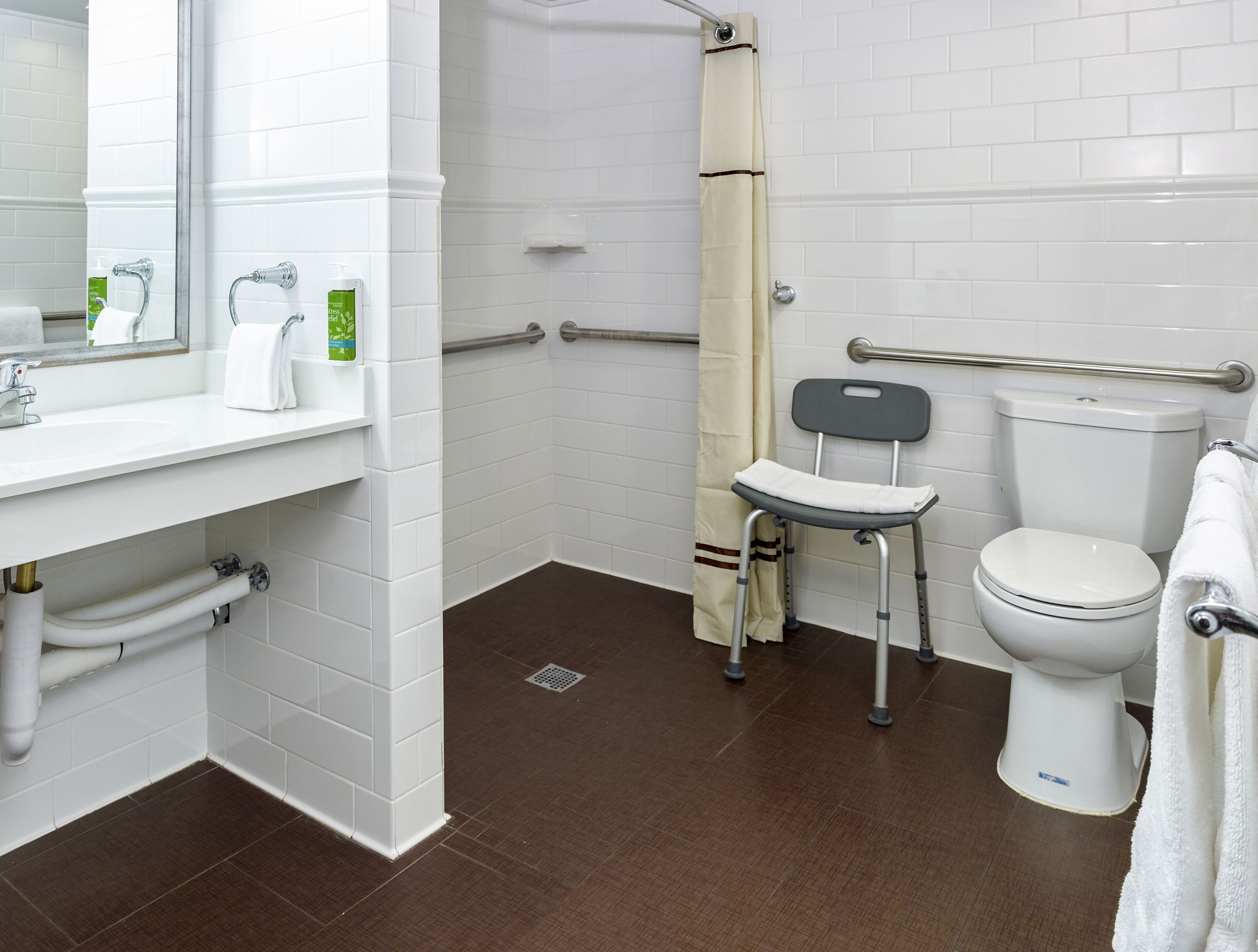 A bathroom with white tiles, a sink, a toilet, a shower, and a grab bar.