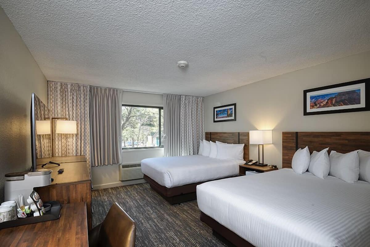 Habitación de hotel con dos camas, un escritorio, una silla, una ventana con cortinas y un cuadro en la pared.