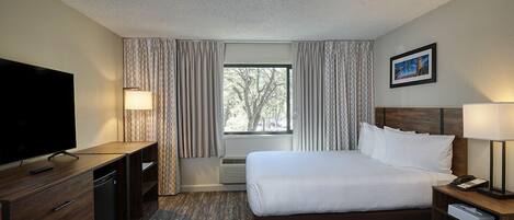 A hotel room with a bed, a TV, a desk, and a window with curtains.