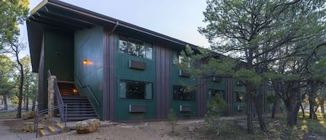 A modern building with a green exterior, a staircase leading to the entrance, and a gravel driveway.
