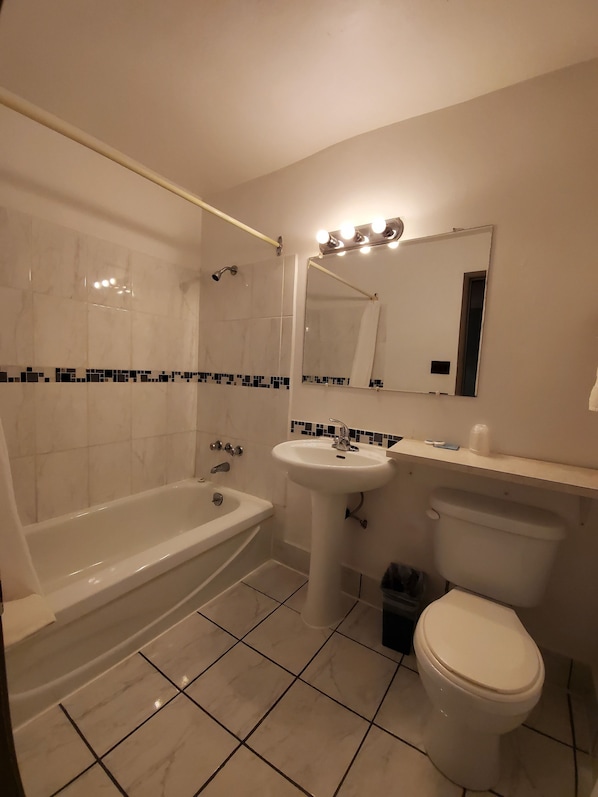 Un baño con bañera, lavamanos, inodoro y espejo con luces arriba.
