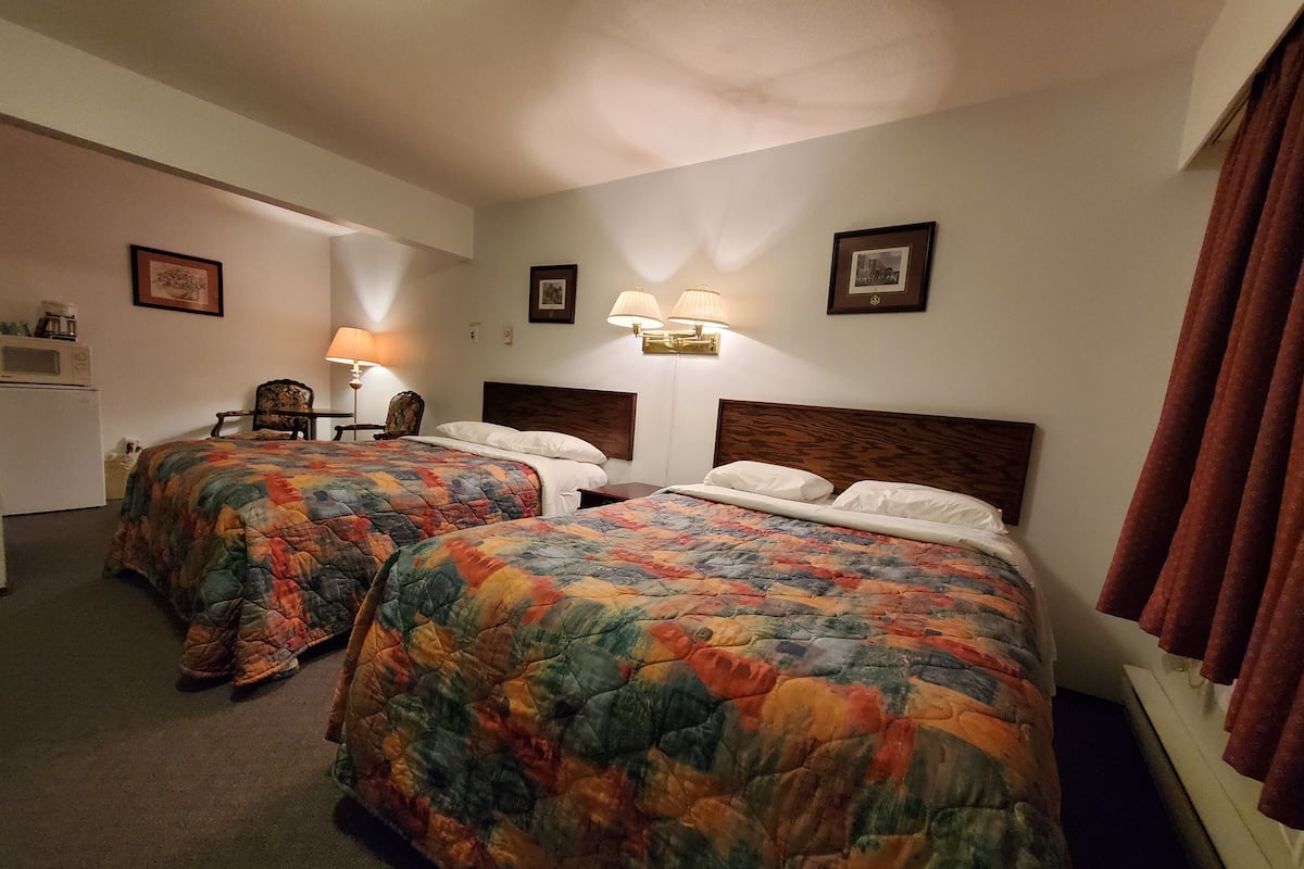 A hotel room with two beds, a desk, a chair, and a microwave.
