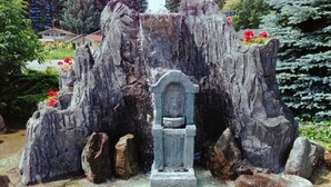 A rock formation with a statue in the center, surrounded by rocks and flowers.