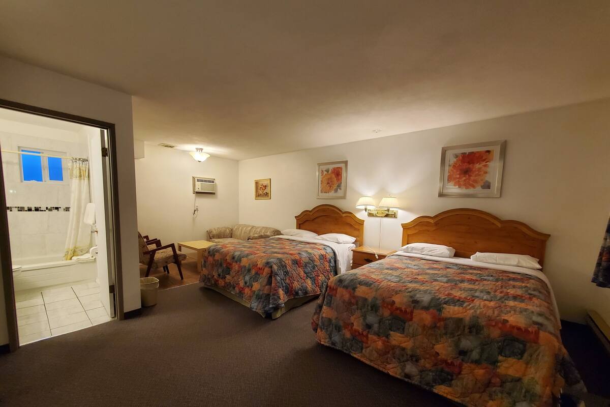 A hotel room with two beds, a bathroom, a desk, and a chair.