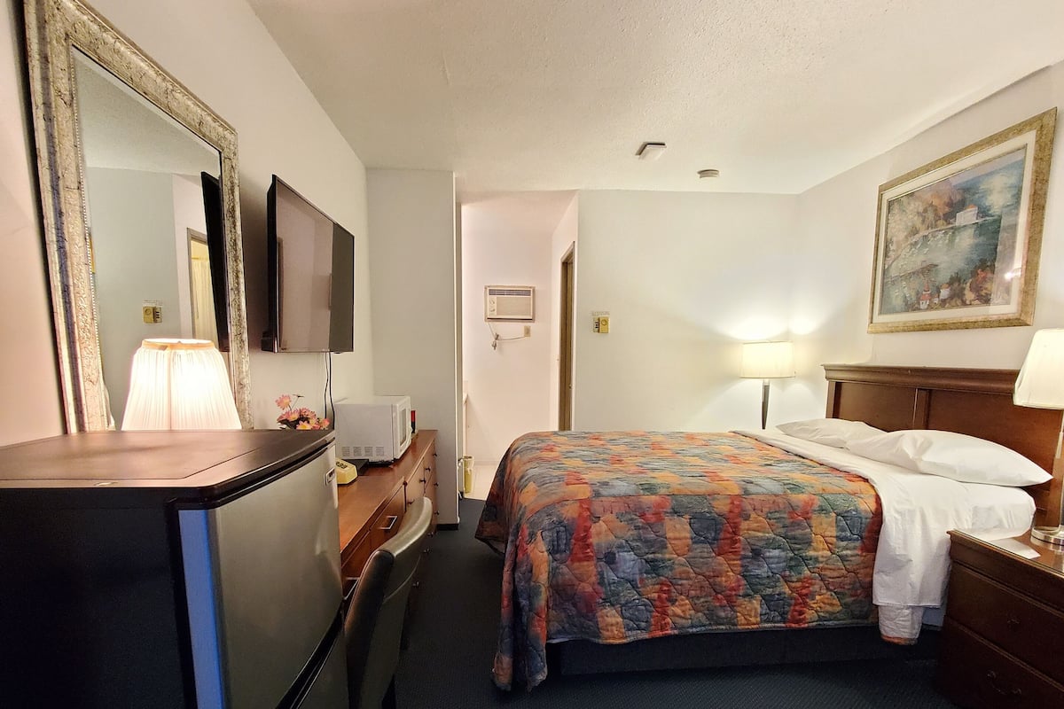 A hotel room with a bed, a desk with a lamp, a television, and a painting on the wall.
