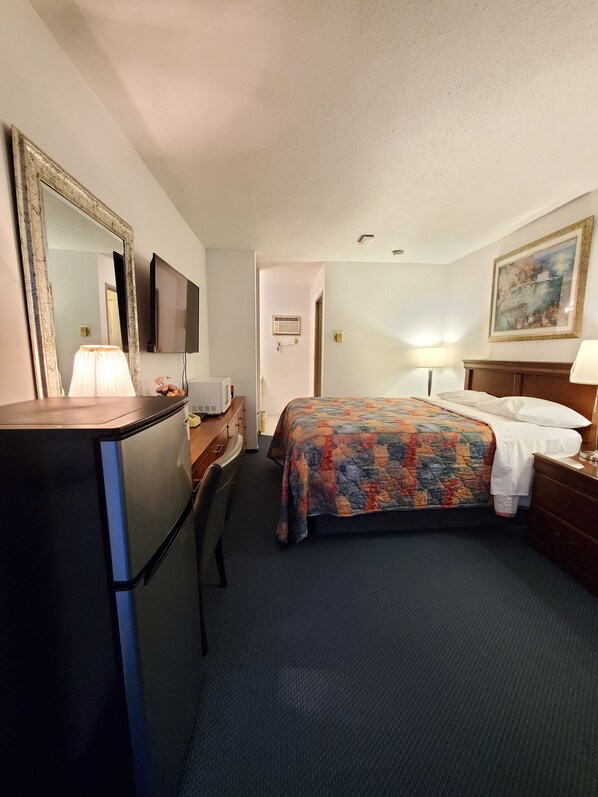 A hotel room with a bed, a desk with a lamp, a television, and a painting on the wall. - Red Roof Motor Inn (Hope)
