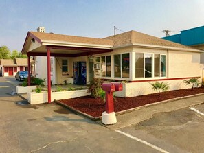 A single-story motel with a covered front porch, a drive-in car park, and a small landscaped area with plants. - Travelers Inn Motel (Salem)
