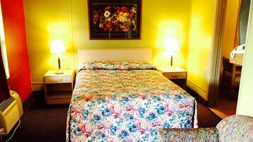 A hotel room with a floral bedspread, two bedside lamps, a painting on the wall, and a chair.