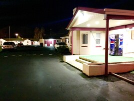 Un motel con una zona de estar al aire libre cubierta, una máquina expendedora y un estacionamiento con varios autos.