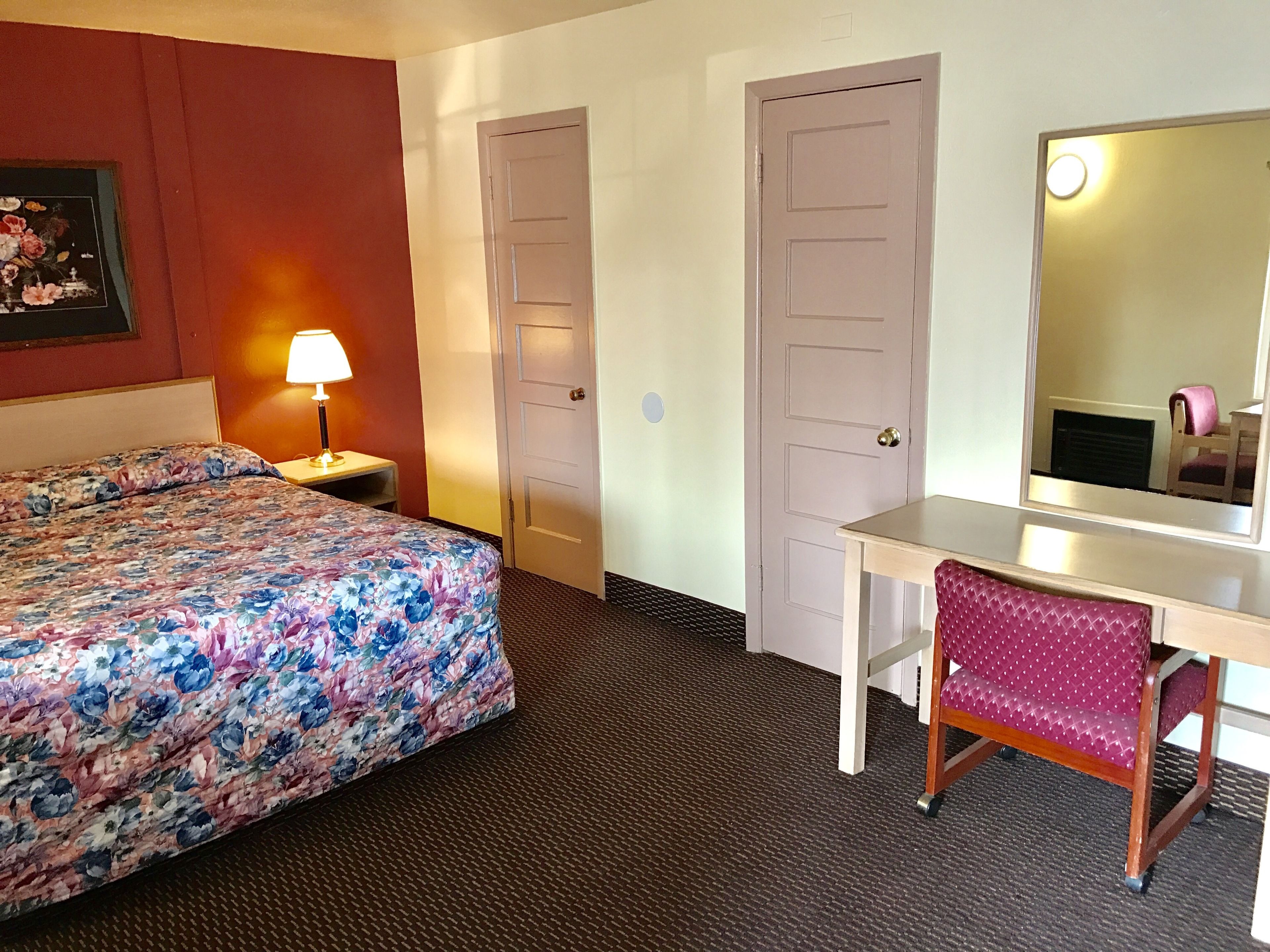 Une chambre d’hôtel avec une couvre-lit à motifs floraux, un bureau avec une chaise, une lampe et deux portes.