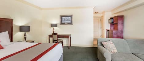 A hotel room with a bed, a desk, a chair, a sofa, and a television.