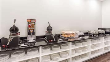 A buffet setup with waffle makers, a coffee machine, and a tray of pastries.