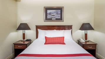 Une chambre d’hôtel avec un grand lit, deux tables de chevet avec des lampes, un tableau encadré au mur et un oreiller rouge.