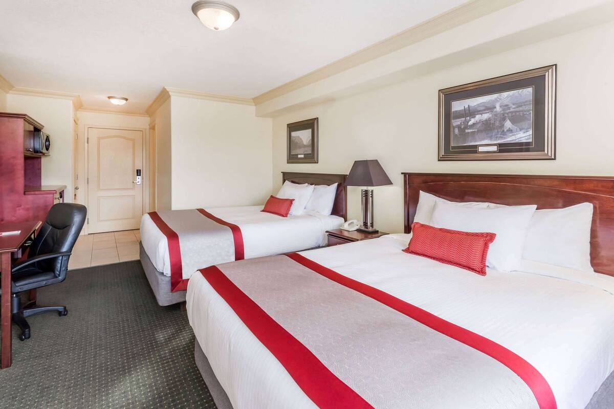 A hotel room with two beds, a desk, a chair, a lamp, and a framed picture on the wall.