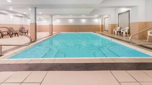 Una piscina con plataforma de baldosas, sillas y un vestuario con puerta.