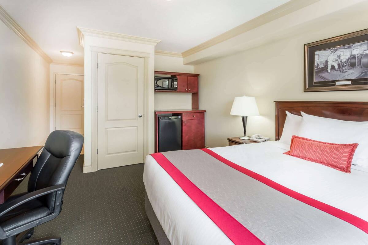 A hotel room with a bed, a desk, a chair, a microwave, and a framed picture on the wall.