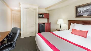 Een hotelkamer met een bed, een bureau, een stoel, een magnetron en een ingelijst kunstwerk aan de muur.