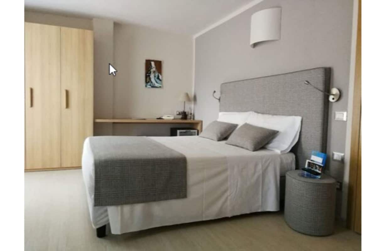 A neatly arranged bedroom with a large bed, bedside table, lamp, and a small round table with a book.