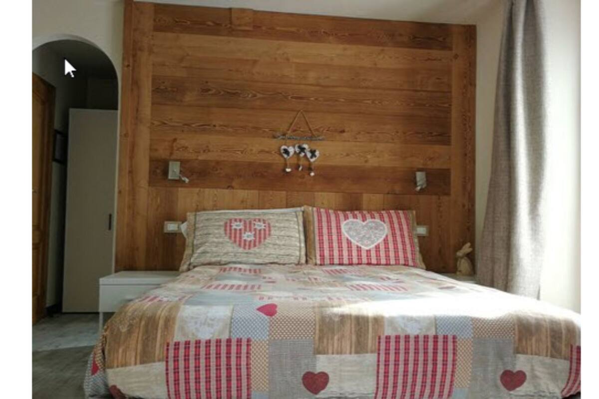 A bedroom with a wooden headboard, a quilted bedspread with heart patterns, and a small hanging decoration.