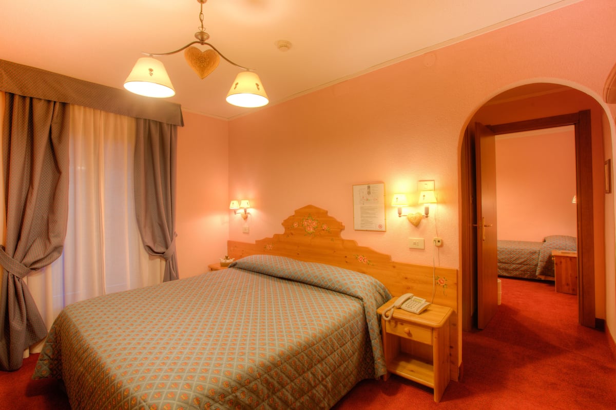A hotel room with a bed, bedside table, lamp, and a door leading to another room.