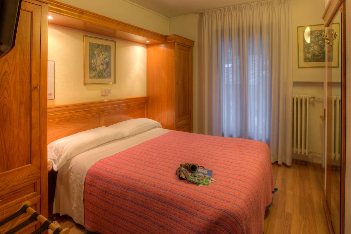 A hotel room with a wooden headboard, a bed with a red and white bedspread, a framed picture on the wall, and a window with curtains.