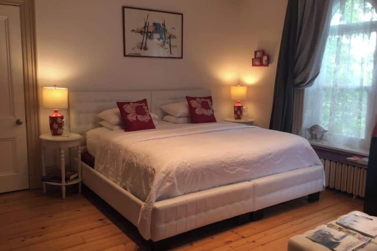Ein Schlafzimmer mit einem großen Bett, zwei Nachttischen mit Lampen, einem Bild an der Wand und einem Fenster mit Vorhängen.