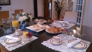 Una mesa de desayuno servida con platos, tazas y una variedad de alimentos, entre ellos, pasteles y fruta.