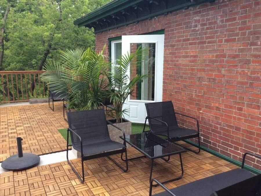 Un patio con dos sillas negras y una mesa, rodeado de un muro de ladrillo y follaje.