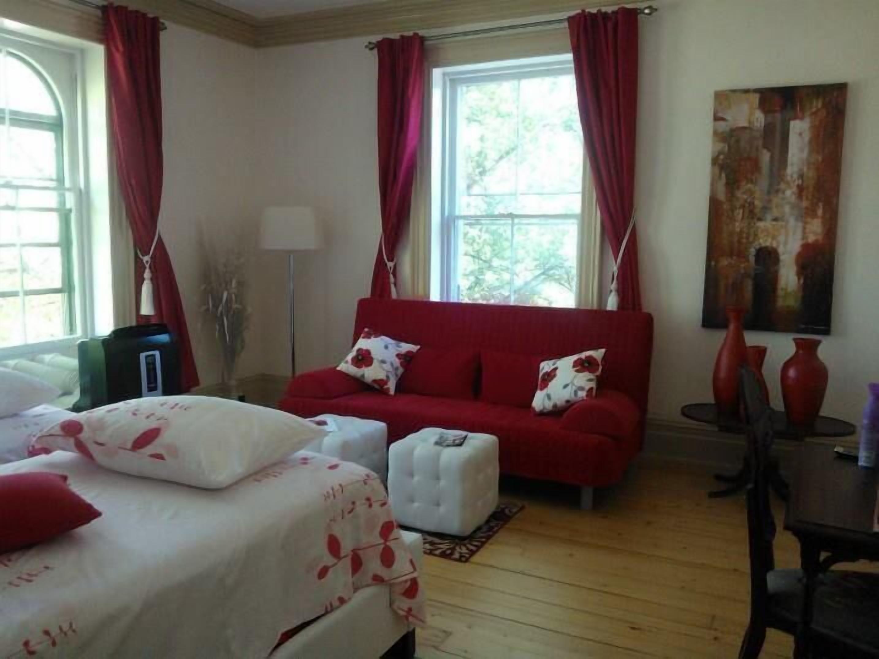 A hotel room with a bed, a red sofa, a white ottoman, and a painting on the wall.